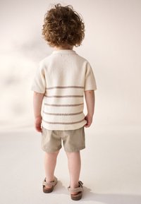 Kremowy, dzianinowy krótki rękaw z brązowymi poziomymi paskami, zestawiony z jasnobeżowymi szortami i brązowymi sandałami.
