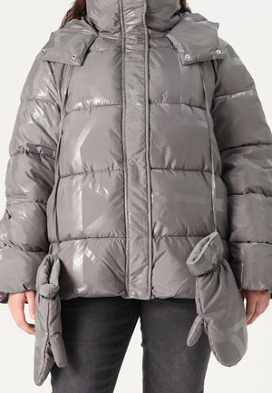 Luchtig grijs winterjack met aangehechte wanten aan de mouwen, gedragen door een persoon in donkere broek.