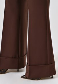 Pantalons marron à jambe large en tissu lisse avec une coupe ajustée, dotés d'un ourlet replié. Assortis à des talons noirs pointus avec des accents en écaille de tortue.