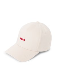 Cremefarbener Baseball-Cap mit einem gebogenen Schirm, der auf der Vorderseite das rot gestickte "HUGO"-Logo zeigt. Hergestellt aus einem strukturierten Stoff mit genähten Akzenten.