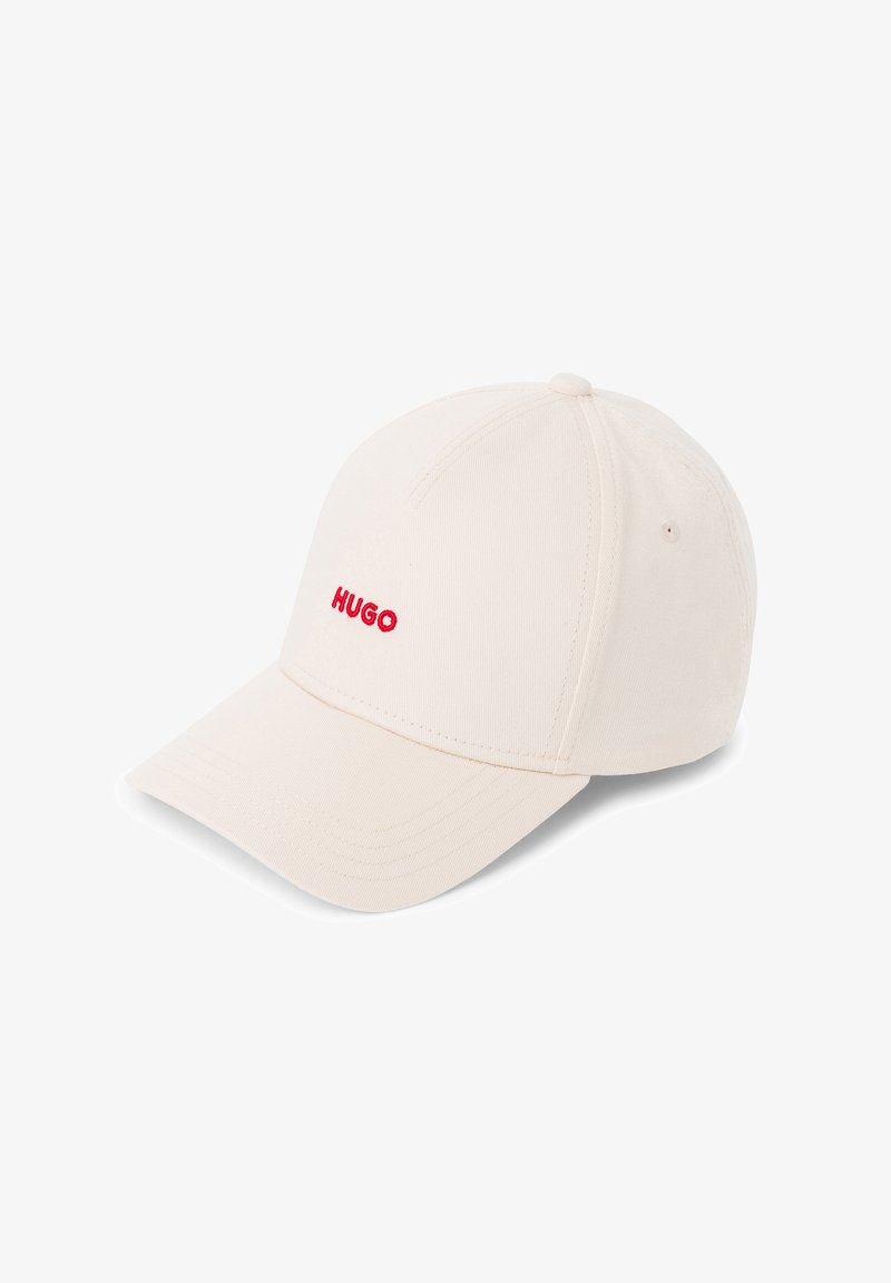 Cremefarbener Baseball-Cap mit einem gebogenen Schirm, der auf der Vorderseite das rot gestickte "HUGO"-Logo zeigt. Hergestellt aus einem strukturierten Stoff mit genähten Akzenten.