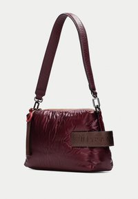 Sac à main bordeaux avec une finition texturée et froissée. Doté d'une bandoulière en cuir brun foncé et d'une fermeture éclair. Forme rectangulaire compacte.