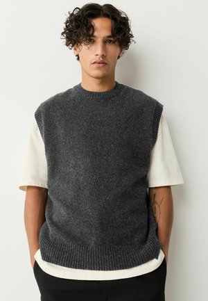 Gilet sans manches en laine grise avec un col et un ourlet à côtes, superposé sur une chemise crème à manches courtes, sur un fond neutre.