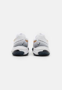 Baskets de sport blanches avec une tige en mesh texturé et des accents gris, dotées d'une semelle foncée et d'un logo en relief sur le talon.