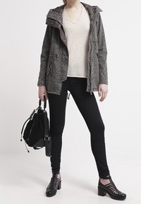 Gray patterned jacket with a hood, beige v-neck top, black skinny pants, and black strappy heeled shoes. Black handbag with straps.