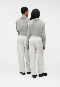 Δύο άτομα με την πλάτη γυρισμένη, φορούν αντίστοιχα γκρι πλεκτά μπλουζάκια και ανοιχτόχρωμα γκρι παντελόνια φόρμας. Τα παντελόνια έχουν ελαστική ζώνη μέσης και τσέπη.