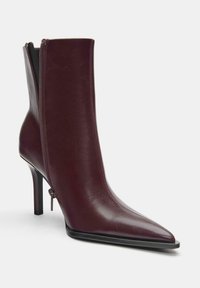 Bordeauxfarvet læderankelstøvle med spids tå, lynlås i siden, slank stiletthæl og tekstureret finish. Sort sål fremhæver designet.