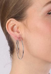 Zilveren hoepeloren, groot, gepolijst, cirkelvormig ontwerp, hangend aan het oor. Gladde textuur, lichtgewicht, subtiel reflecterend licht.