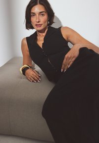 Musthave muströömiga must sõrmkingadega top, mis on kombineeritud lahtiste mustade pükstega. Mudel toetub tekstuursele heledale hallile kangale.