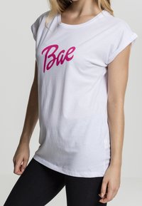 Witte katoenen T-shirt met opgerolde mouwen en een roze grafische print van het woord "Bae" op de voorkant. Casual pasvorm, zachte textuur.