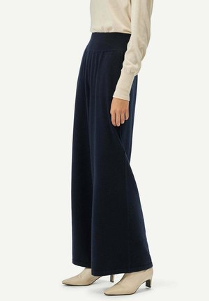 Pantalons larges bleu marine en tissu doux, dotés d'une taille haute et d'une texture lisse, accompagnés de manches ajustées de couleur crème.