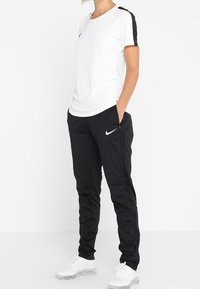 Nike sportklädesset med en vit t-shirt med korta ärmar och svarta detaljer samt svarta byxor, tillverkade i andningsbart material. Vita sneakers fulländar looken.