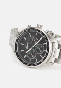 Montre en acier inoxydable argenté avec un cadran noir, trois sous-cadrans, des accents verts et une échelle tachymétrique. Comprend un bracelet en métal.