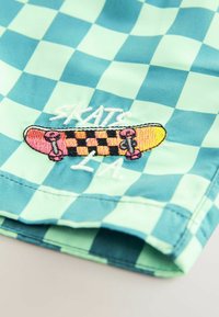 Ternede blå og grøn stof med en broderet skateboard-design i pink og sort med hvid tekst, der siger "SKATS LA."