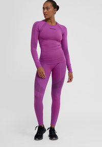 Paarse sportieve longsleeve top en bijpassende leggings van een gladde, rekbare stof met textuurdetails, gecombineerd met zwarte sportschoenen.