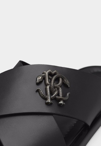 Μαύρο δερμάτινο σανδάλι slide με επικαλυπτόμενους ιμάντες και υφασμένο μεταλλικό έμβλημα σε σχήμα φιδιού στο πάνω λουράκι.