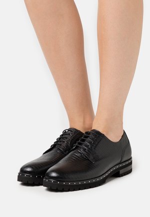 Chaussures noires à lacets en cuir texturé, avec une semelle ondulée et des clous métalliques le long du bord. Design à bout arrondi, finition lisse.