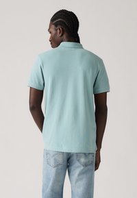 Light blue cotton polo shirt with short sleeves, a collar, and a relaxed fit. Worn with light blue denim jeans.