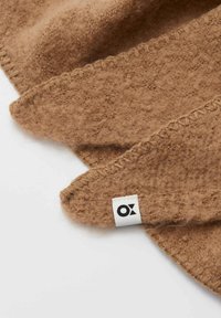 Braune, strukturierte Fleece-Decke mit einem umgeklappten Rand und sichtbaren Nähten. Ein kleines Stoffetikett mit der Aufschrift "OX" ist angebracht.