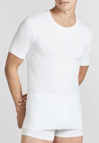 T-shirt bianco a maniche corte realizzato in tessuto morbido ed elastico. Ha un collo rotondo base e un design aderente, indossato con pantaloni boxer bianchi abbinati.