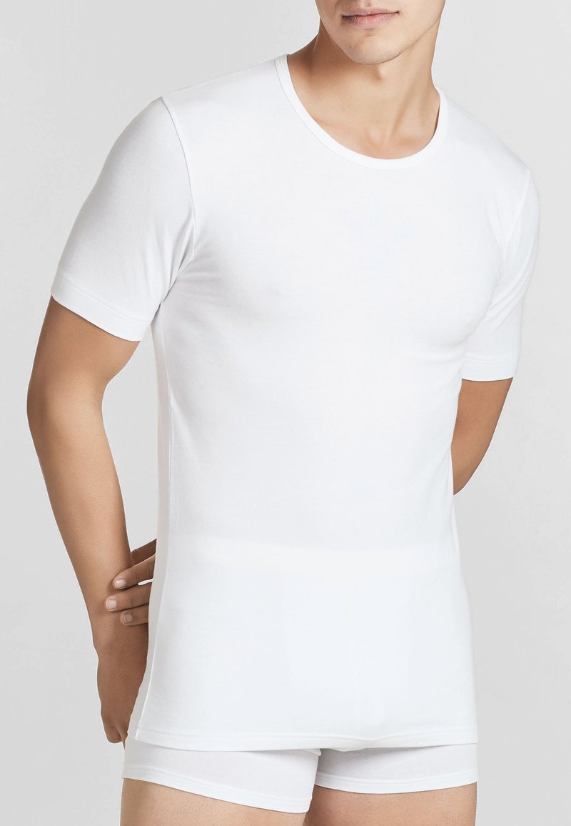T-shirt bianco a maniche corte realizzato in tessuto morbido ed elastico. Ha un collo rotondo base e un design aderente, indossato con pantaloni boxer bianchi abbinati.