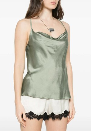 Donna che indossa un camisole in raso verde chiaro e pantaloncini bianchi con bordatura in pizzo nero, accessoriata con una collana con ciondolo.