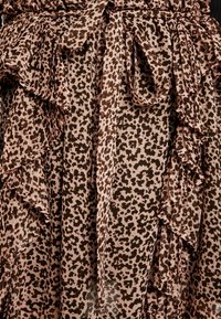 Leopardenmusterstoff mit beigem Hintergrund, der entlang der Kanten Rüschen aufweist und über einen passenden Bindegürtel verfügt. Die Textur wirkt weich und fließend.