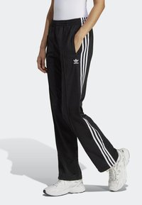 Svarta träningsoverallsbyxor med tre vita ränder längs sidorna, elastisk midja och sidofickor. Tyget verkar slätt och lätt.