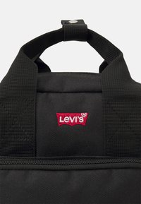 Crna platnena torba s gornjom ručkom, koja sadrži crveno izvezeno "Levi's" logotip i zatvaranje na patentni zatvarač. Izdržljiv i strukturni dizajn.