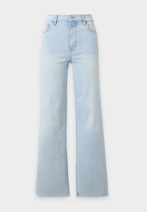 Femme portant un haut marron à manches longues, un jean large bleu clair, des sandales noires à talons hauts, et portant un sac à bandoulière en cuir marron.