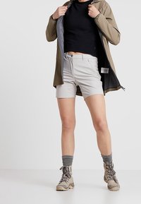 Korta grå shorts, svart kort topp och olivgrön lätt jacka med meshtygsfoder. Bruna vandringskängor och grå strumpor med ribbad struktur.