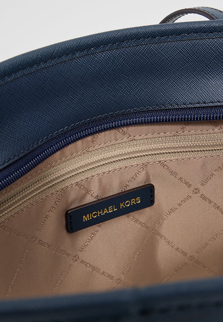 Intérieur d'un sac bleu marine avec une texture lisse, doublure beige avec un motif discret de logo et une poche zippée avec une étiquette dorée.