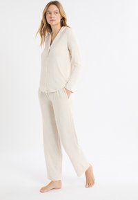 Beżowa, długorękawowa bluzka z zapięciem na guziki, zestawiona z dopasowanymi luźnymi spodniami z elastycznym paskiem w talii i bocznymi kieszeniami.