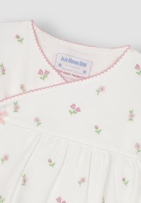 Weißes Babybekleidungsstück aus Stoff mit rosa floralem Stickmuster, gezacktem rosa Saum am Ausschnitt und einem kleinen rosa Band als Akzent.