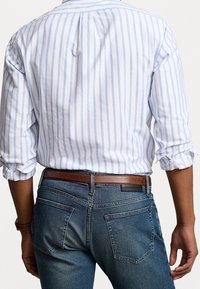 Wit en lichtblauw gestreept shirt met opgerolde mouwen, gecombineerd met donkerblauwe denim jeans en een bruine leren riem.