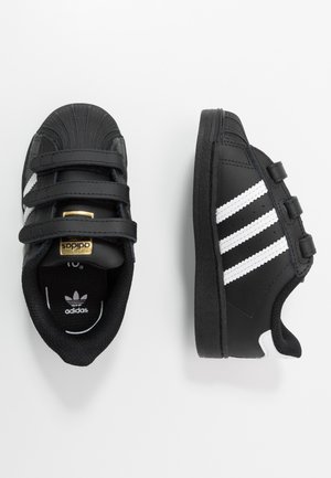 Czarne sneakersy Adidas z białymi paskami, trzema paskami na rzepy i złotym logo na języku, pokazane z góry i z boku na białym tle.