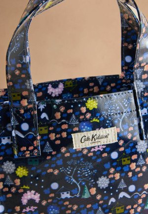 Digitāla tote soma ar tumši zilu rakstu, kas rotāta ar krāsainiem ziedu un ģeometriskiem dizainiem, melniem rokturiem un austā logotipa etiķeti.