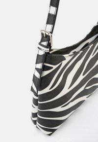 Zebra-Muster-Handtasche aus synthetischem Material, mit schwarzen und weißen Streifen, flacher Form und verstellbarem Tragegurt mit silbernem Zubehör.