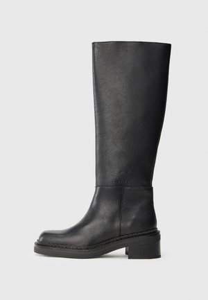 Knee-high must mustelõngat mustast nahast, ümarate varvastega, kergelt tõstetud kand, nähtava õmblusega ja välisküljel reljeefse logo detailiga.