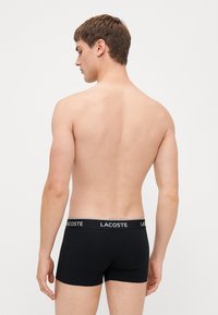 Crne bokserice napravljene od rastezljivog materijala, sa mekim pojasom na kojem je logo Lacoste. Dizajn je minimalistički i prilagođen tijelu.