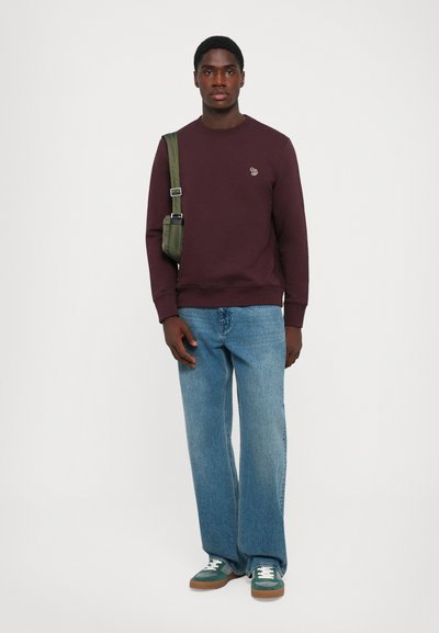 Burgundy sweatshirt with ribbed cuffs, paired with light blue wide-leg jeans and green sneakers, carried with a green crossbody bag.