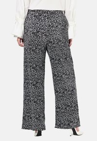 Spodnie o szerokich nogawkach z czarno-białym abstrakcyjnym wzorem, wykonane z lekkiego materiału, z gładką fakturą i elastycznym pasem.