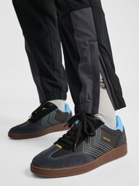 Sorte og grå sneakers med blå detaljer båret med hvide sokker og sorte bukser med ankel lynlåse og elastiske manchetter.