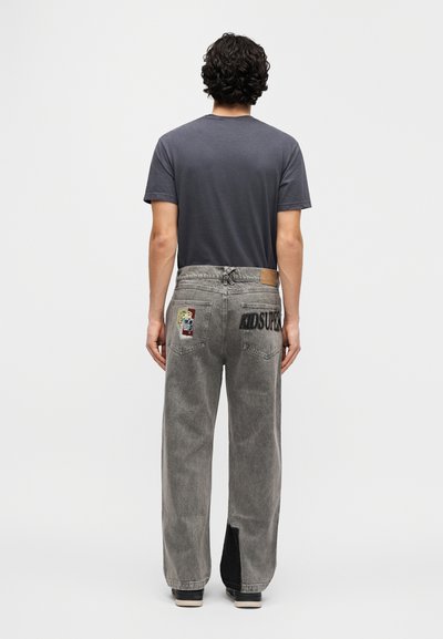 Γκρι τζιν από τζιν υλικό με άνετη εφαρμογή, με λεπτομέρειες από μπαλώματα και το κείμενο "AIDSUPRE" στην πίσω τσέπη. Μαύρη υφασμάτινη λεπτομέρεια στο τελείωμα.