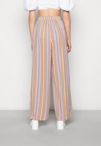 Vida byxor i lätt tyg, med ett flerfärgat zigzag-mönster i rosa, gult och grönt, samt ett elastiskt midjeband.