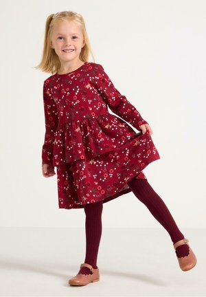 Rode bloemenjurk met lange mouwen en gelaagde rok, gecombineerd met kastanjebruine geribde maillots en lichtroze schoenen met golfranden.