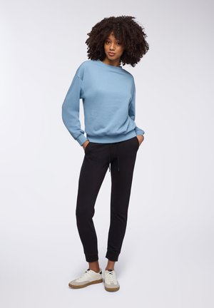 Maglione azzurro chiaro con collo a giro e polsini a costine, abbinato a pantaloni jogger neri e sneaker bianche con dettagli marroni.