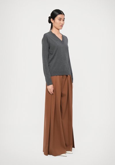 Grijze v-hals trui van zacht materiaal gecombineerd met bruin hoge taille, geplooide broek met wijde pijpen, aangevuld met witte puntige schoenen.