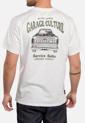 Homme portant un t-shirt blanc avec un motif vintage de camion et de moto et le texte "Garage Culture, Service Suits, Daytona 73" dans le dos.