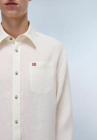 Camicia button-up beige chiaro in lino. Presenta una tasca sul petto con una piccola toppa della bandiera norvegese e bottoni metallici lucidi.